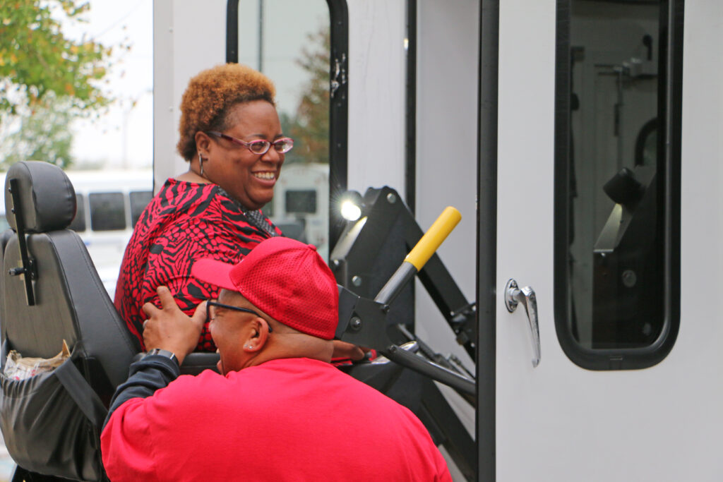A man helping a woman load into a paratransit vehicle using a lift.